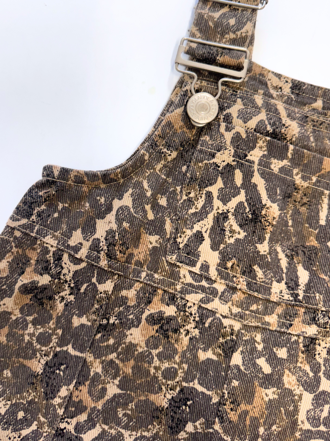 Close-up of the BLYTHE LEOPARD DUNGAREE BABY—denim baby overalls with a leopard print, metal buckle, and button. A cute unisex essential for any occasion.