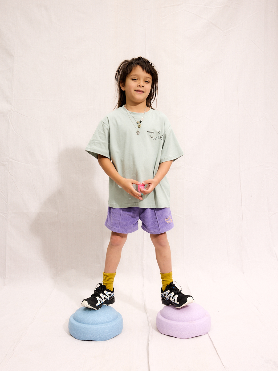 A child is wearing purple Everyday Terry Shorts with the mint Milk Teeth tee