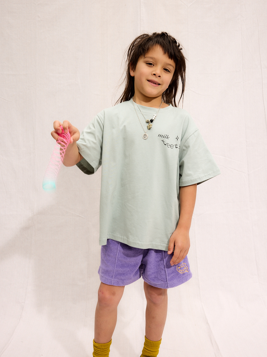 A child is wearing purple Everyday Terry Shorts with the mint Milk Teeth tee