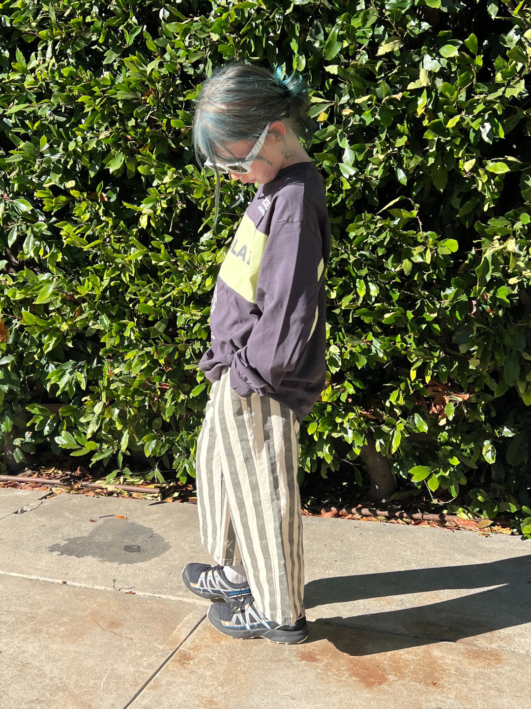 Charcoal Stripe | Person wearing a charcoal sweatshirt with a yellow logo and striped pants standing against a green bush.