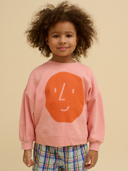 Second image of A pink BOXY POTATO SWEATSHIRT by OXOX CLUB, made from organic cotton, features a simple orange face graphic on the front and is displayed laid flat on a white background.