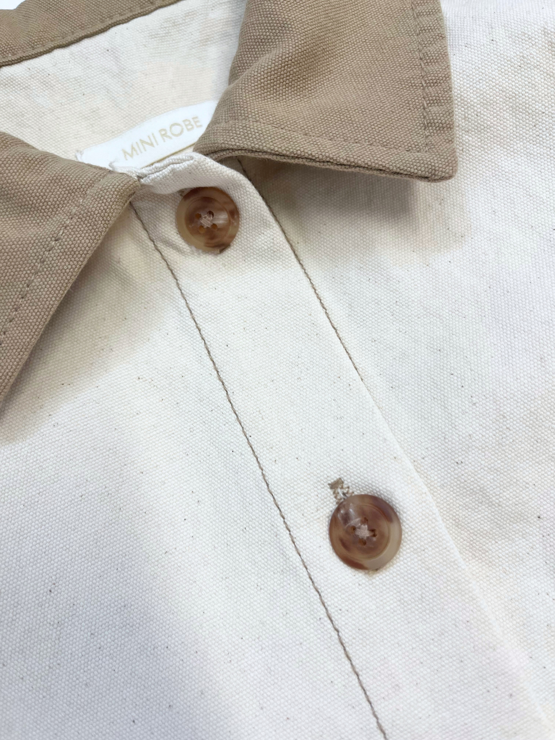 Ecru | Close-up of the MINI WORKWEAR JACKET: a beige collared piece with brown buttons and a "MINI ROBE" tag, styled like a smart jacket that's perfect for kids' workwear-inspired looks.