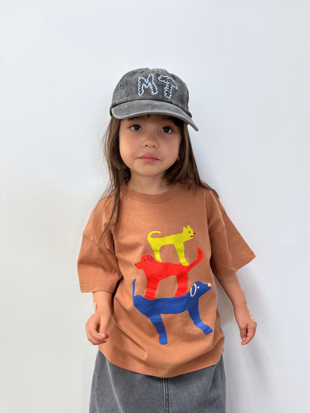 Mocha | Child wearing a brown t-shirt with colorful cat designs and a gray cap on a white background