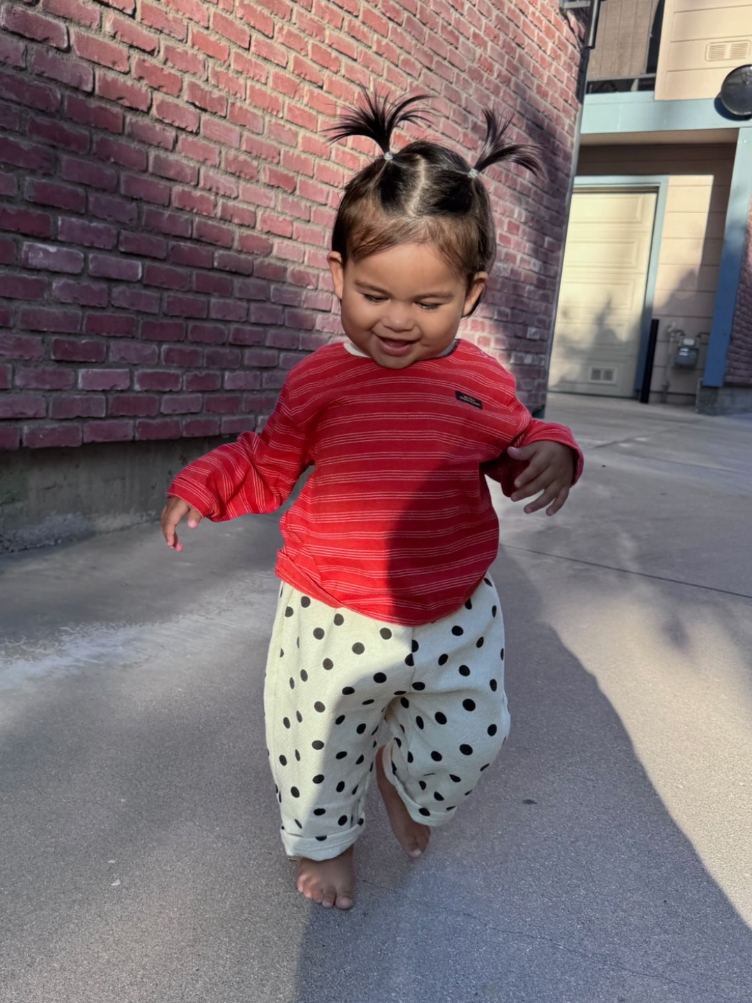 Red | Child in red striped shirt and polka dot pants walking on a sidewalk.
