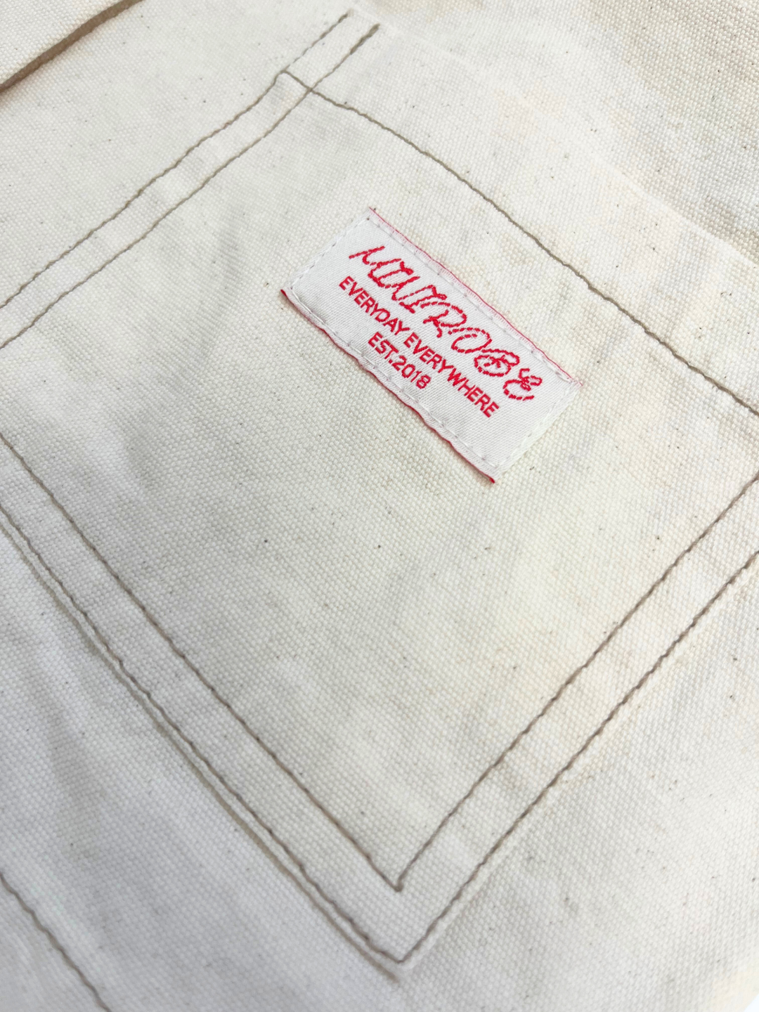 Ecru | Close-up of the MINI WORKWEAR JACKET's cream fabric pocket, showing a white and red "Mimimog, Everyday Everywhere, Est. 2019" label.