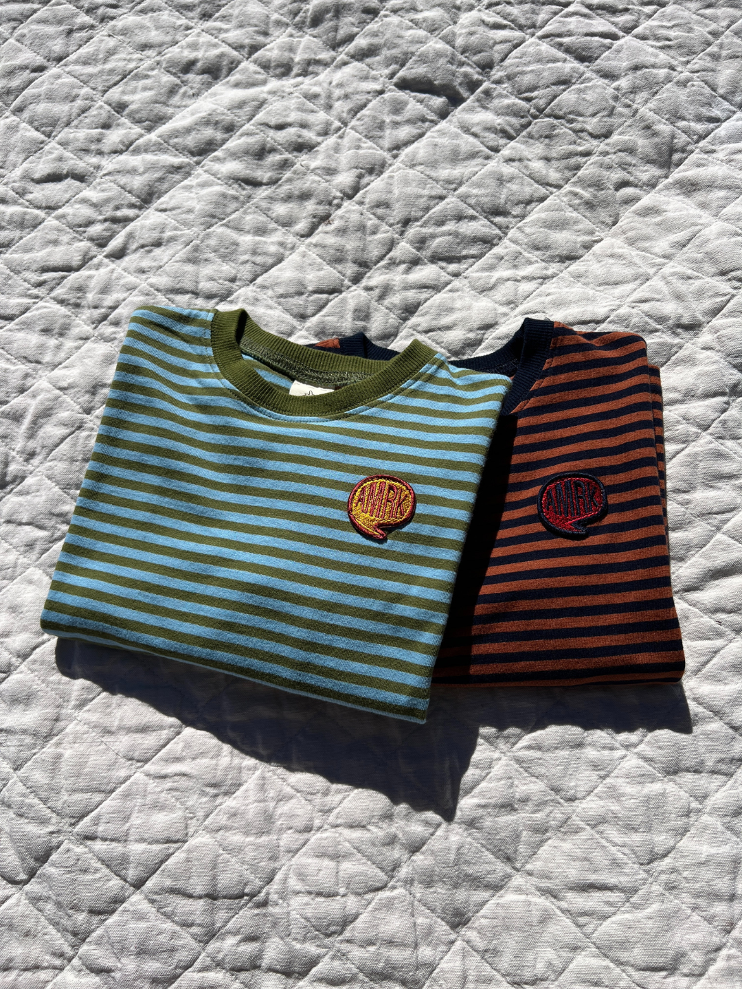 Rust/Navy | Comma Striped Longsleeve in Sky/Olive and Rust/Navy laid on blankets