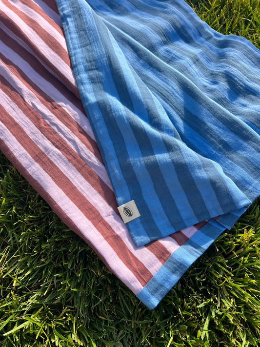 Second image of Blue Stripe | A medium blue and darker blue striped cotton quilt is shown rolled up with a white Milk Teeth label around the middle.
