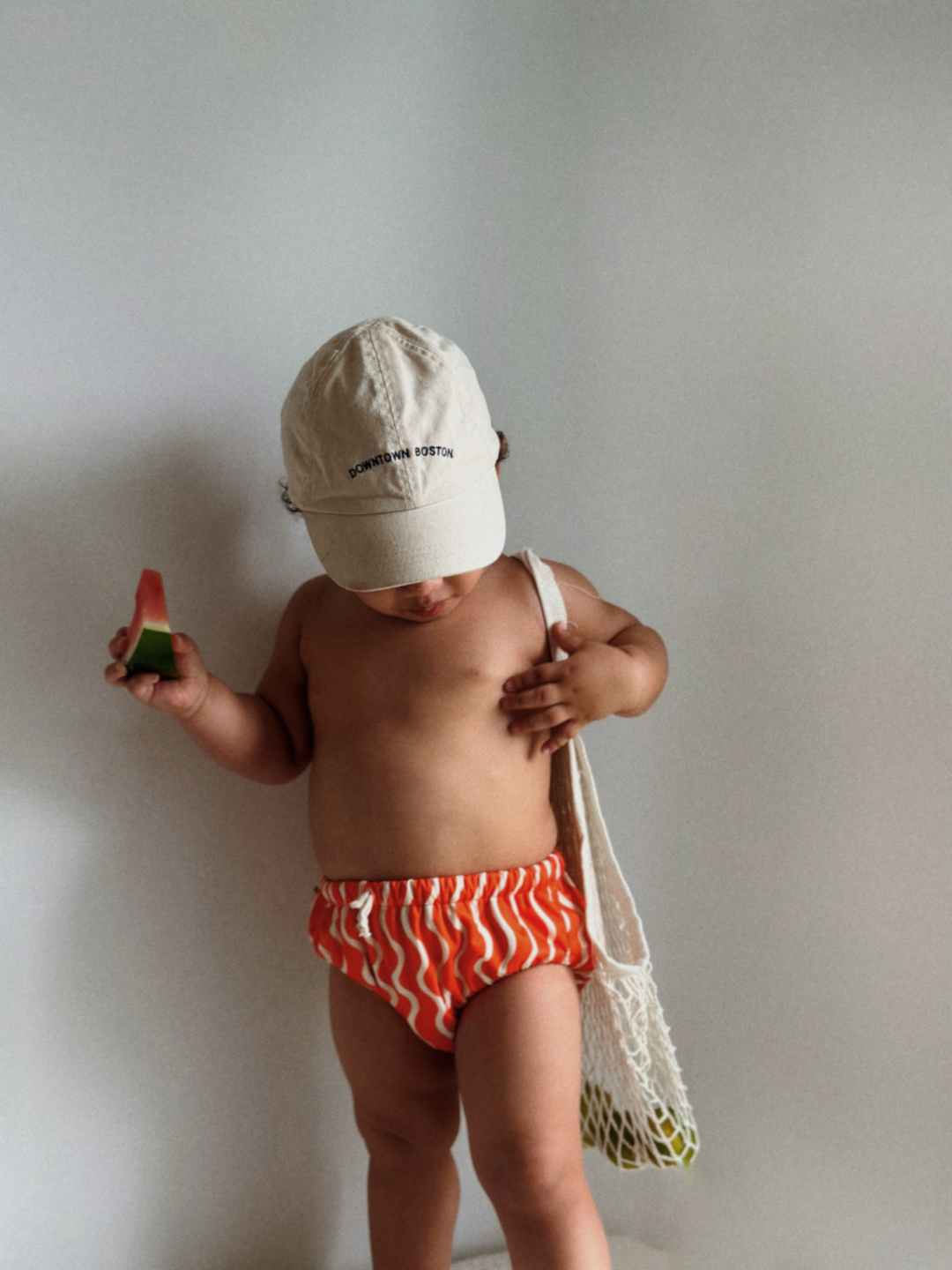 The front view of the swim diaper with an elastic waist with a tie and elastic leg holes on a child. The diaper is a bright orange with wavy and vertical cream colored lines.