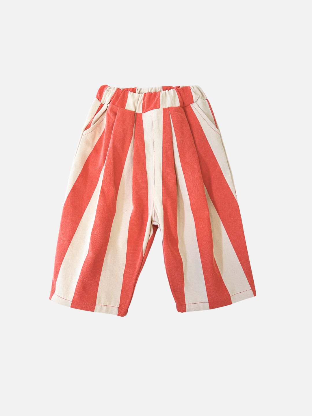 Faded Red | The BIG STRIPE PANTS for children, featuring summery faded red and white wide-leg stripes, come with an elastic waistband and side pockets, crafted from lightweight cotton canvas against a plain background.