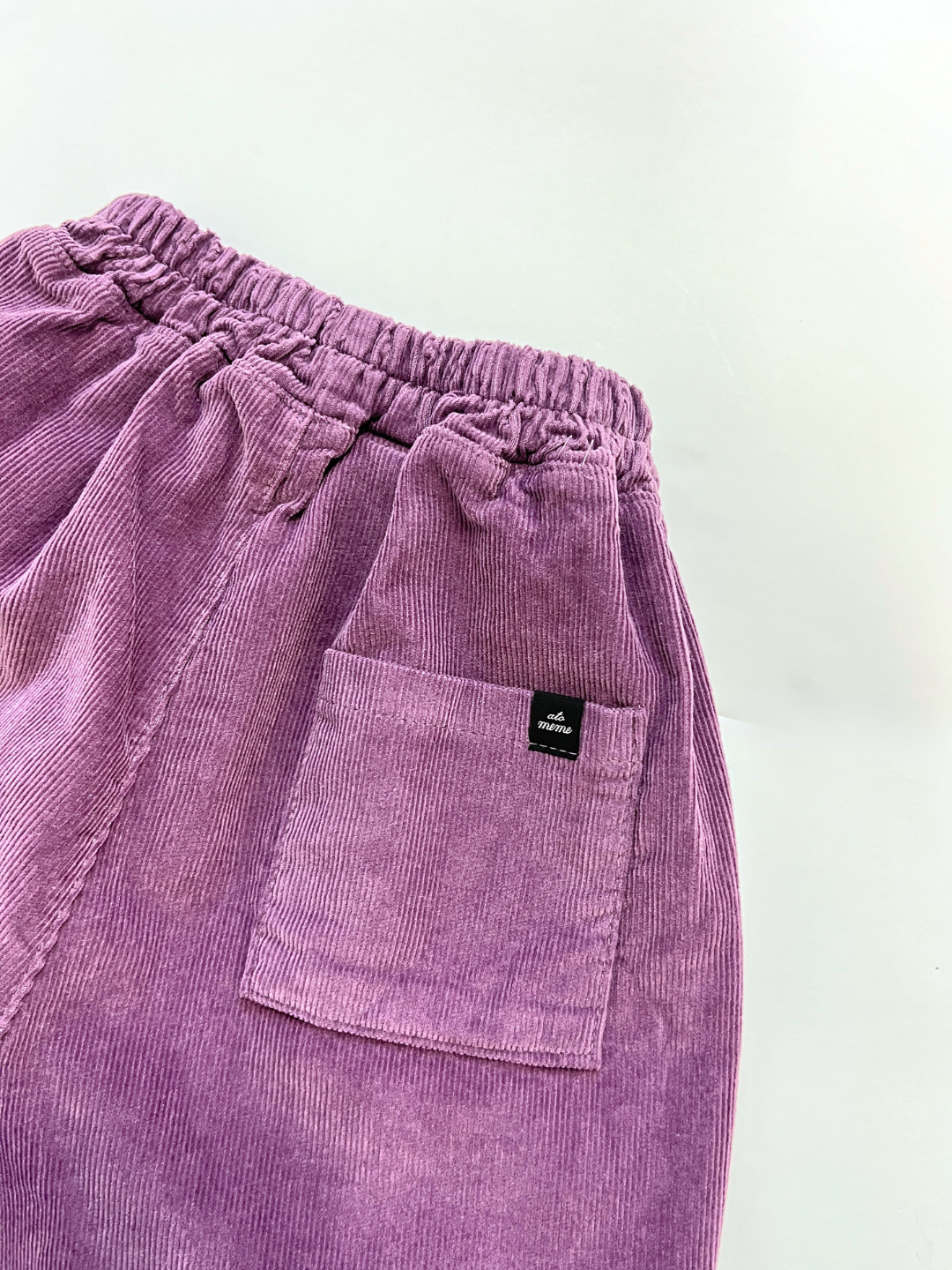 Close-up of comfy CORDUROY PANEL PANT in purple cotton corduroy, featuring an elastic waistband and a back pocket with a small black label from a Korean kids brand.