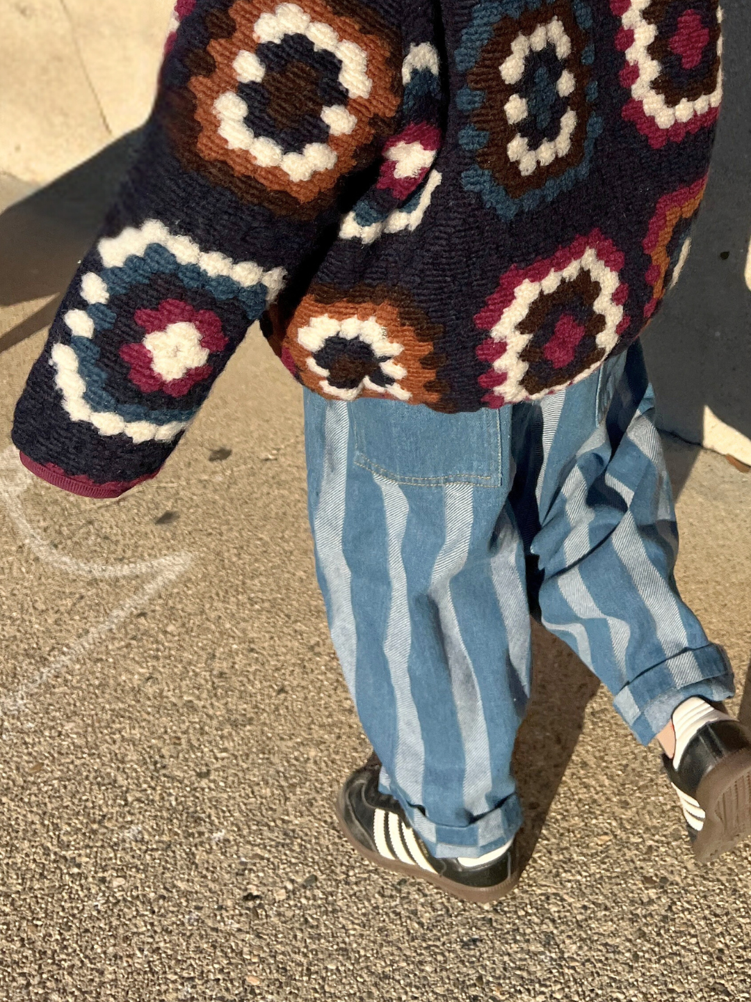 Medium Wash | A child wearing a colorful, patterned sweater and the Stripe Double Trouble Jeans with an elasticated waist strolls on a sunlit pavement.