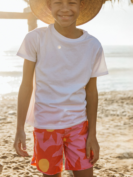 Second image of A front view of the kid's Siesta Scallop Retro Flare Boardshort, highlighting the adjustable waistband white, Saesta Swim logo on the left in pink. The design features large red flowers. 