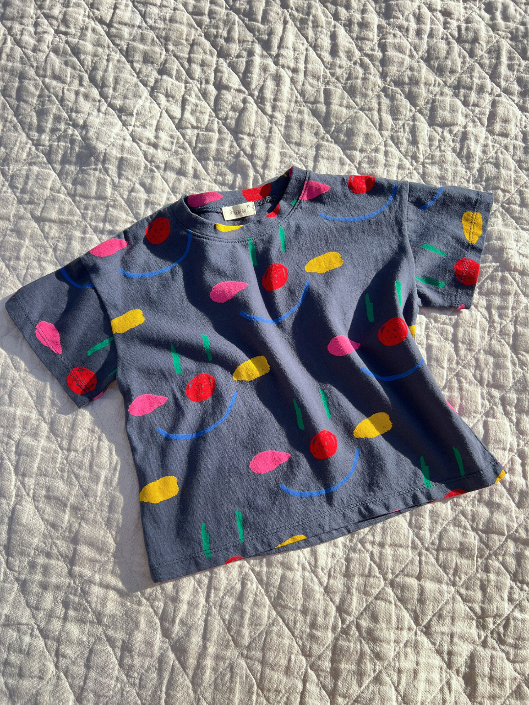 Navy | A kids' Facepaint Tee in Navy laid flat on a quilt in the sun