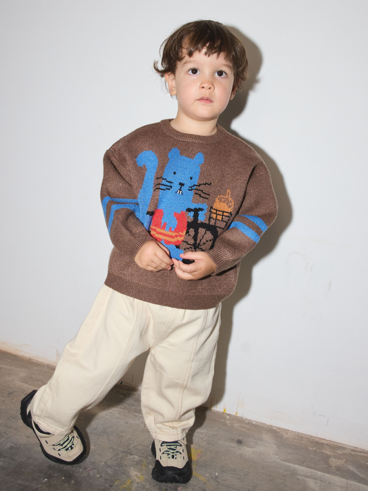 Second image of A brown knit sweater for kids featuring a blue squirrel riding a black bicycle with an acorn in the basket. The sleeves have two blue stripes, and the sweater is shown flat against a light gray background.