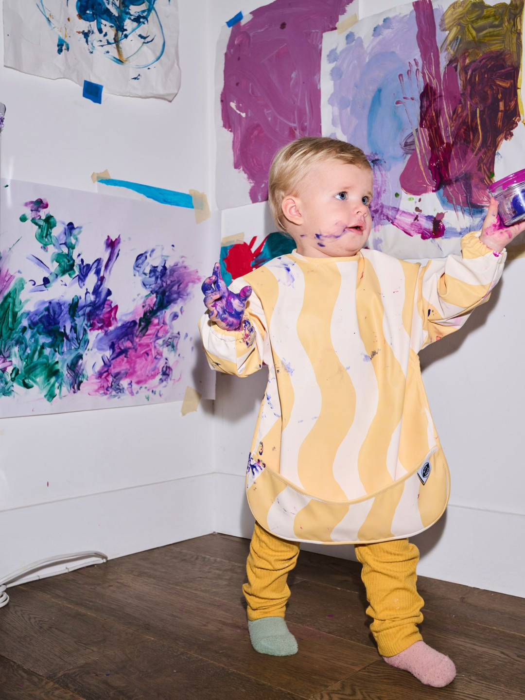 Butter Waves | A child wearing the long sleeve yellow and white wavy bib and a front pocket.