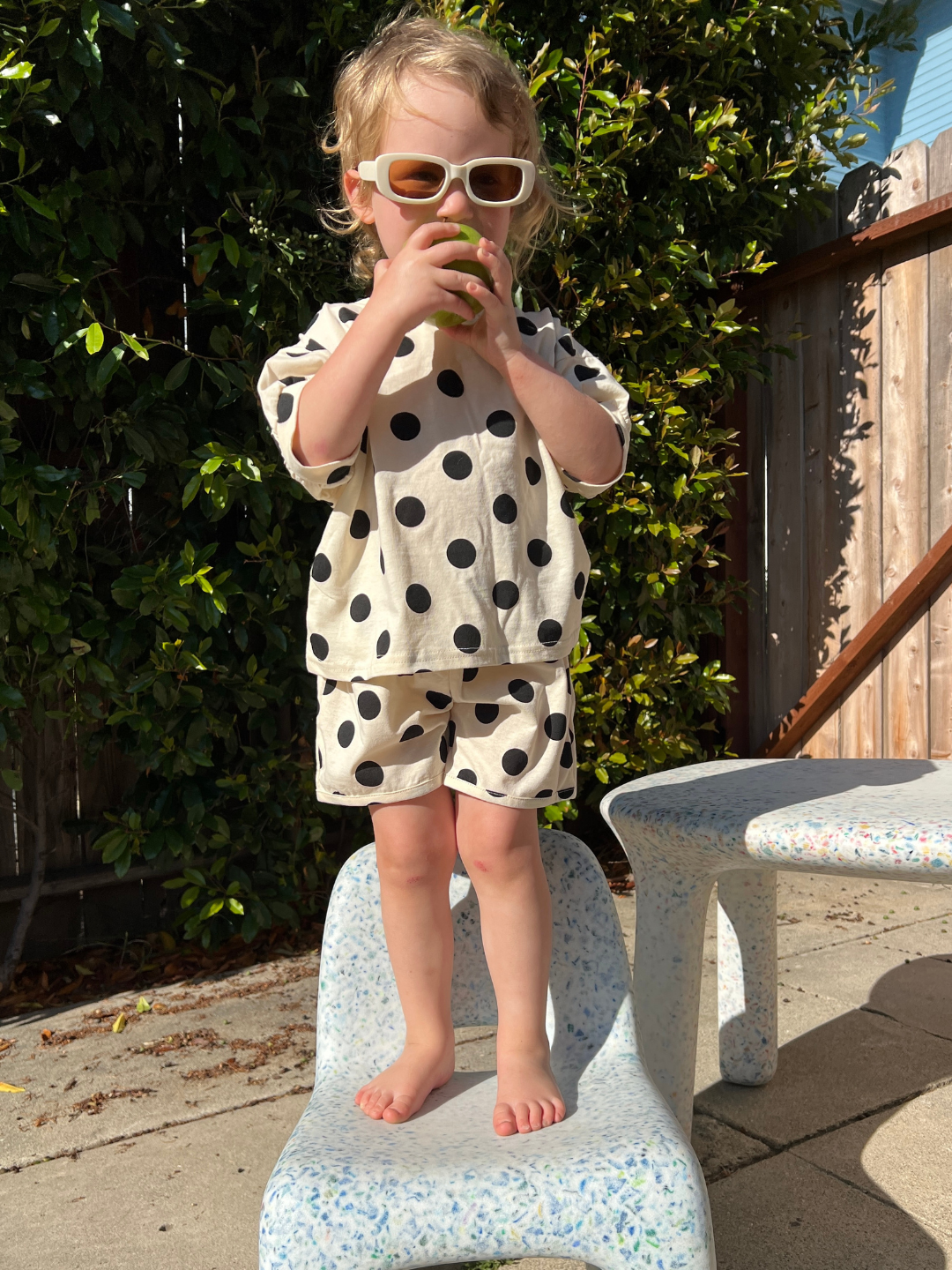 A toddler standing on a chair, wearing a kids' tee shirt and shorts set in a pattern of black dots on an ecru background