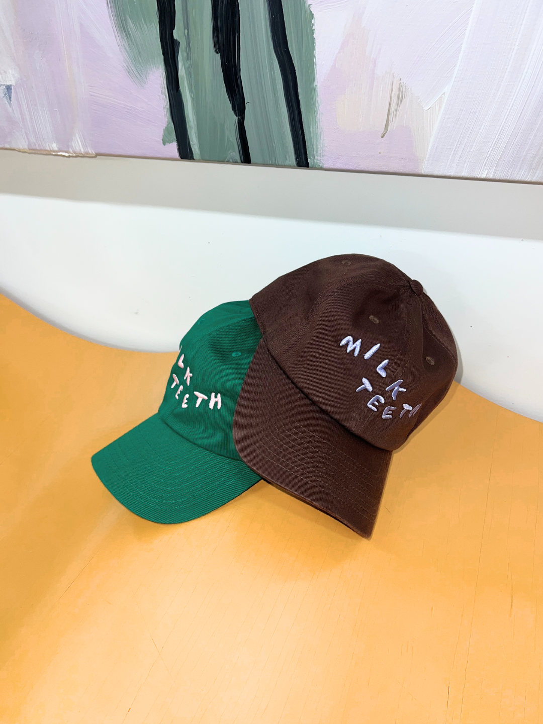 Kelly Green | Milk Teeth adult baseball caps stacked on top of an orange wavy bench.