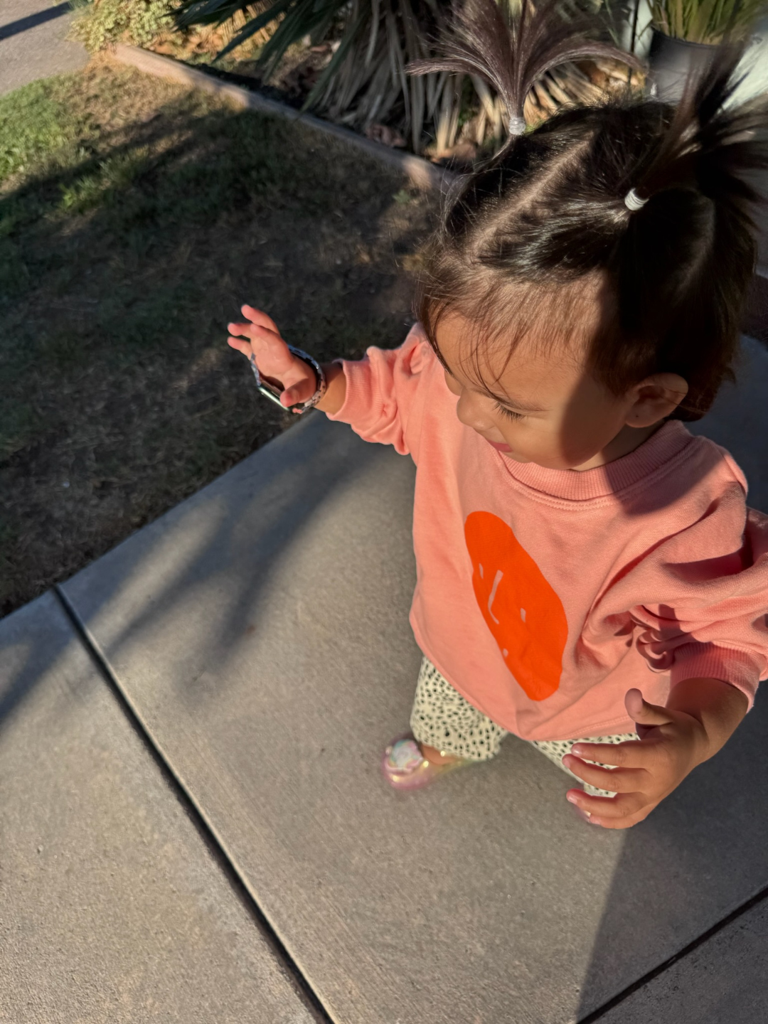 Child wearing a pink sweatshirt with an orange logo on a sidewalk