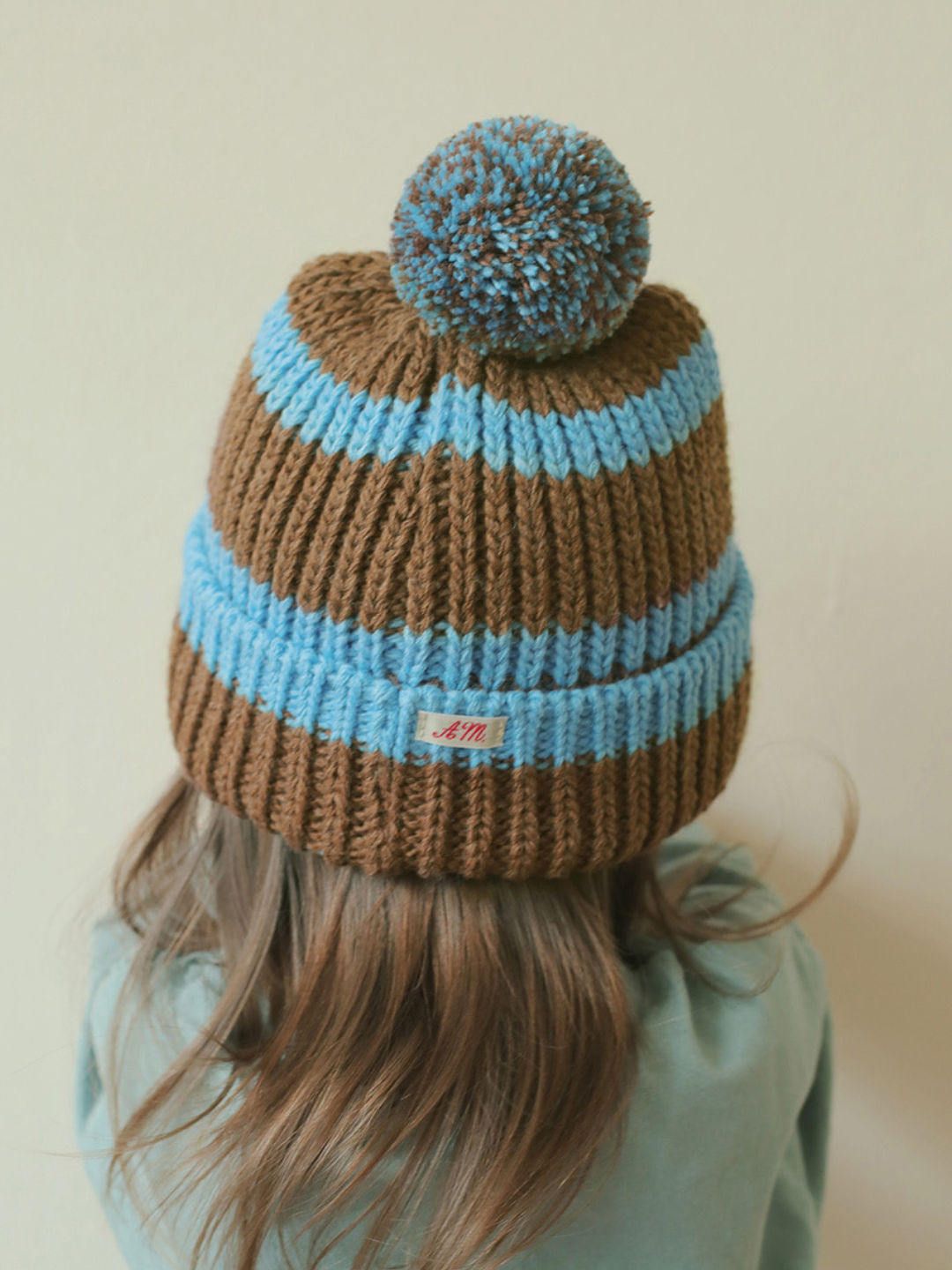 Blue | A child is wearing the blue pompom hat.