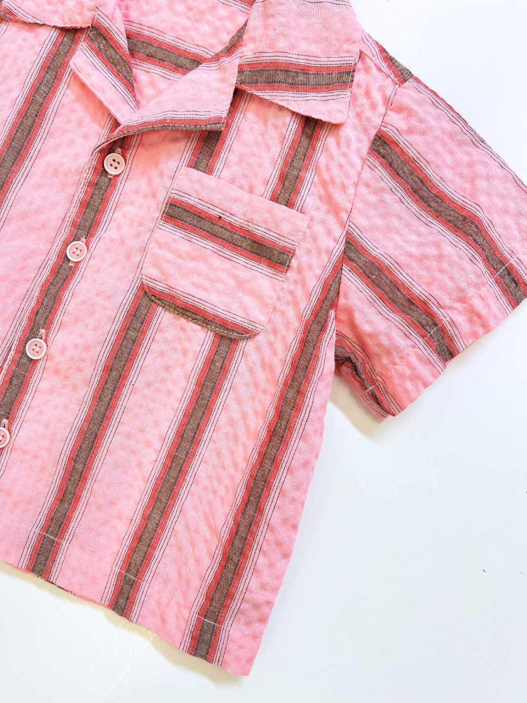 The HAVANA STRIPE SHIRT is a vintage-inspired, short-sleeved pink cotton shirt with red and gray vertical stripes, a notched collar, and a chest pocket, displayed flat on a white background.