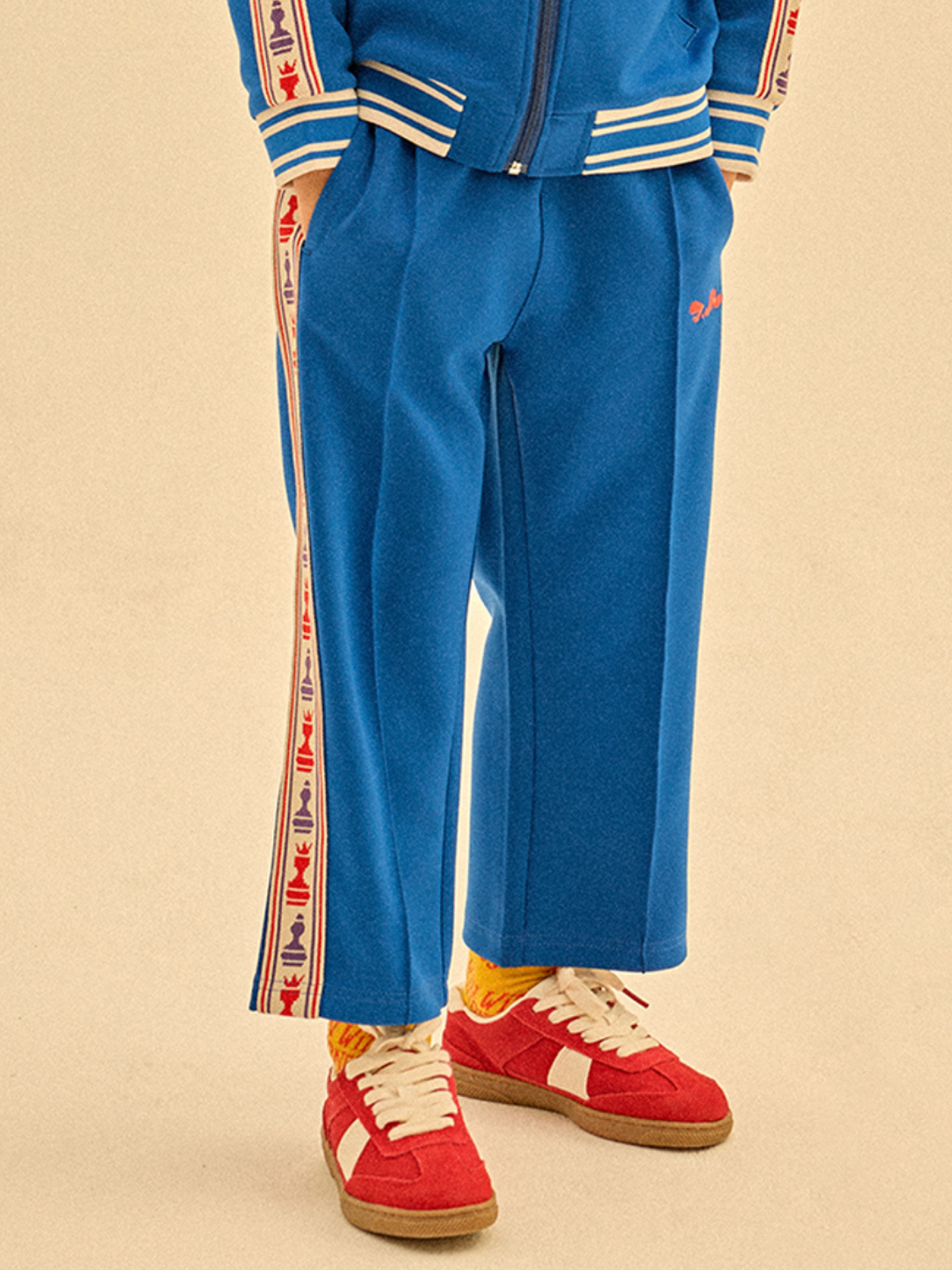 Blue | Wearing CHESS TRACK PANTS with red, white, and blue side stripes, paired with red sneakers and orange socks