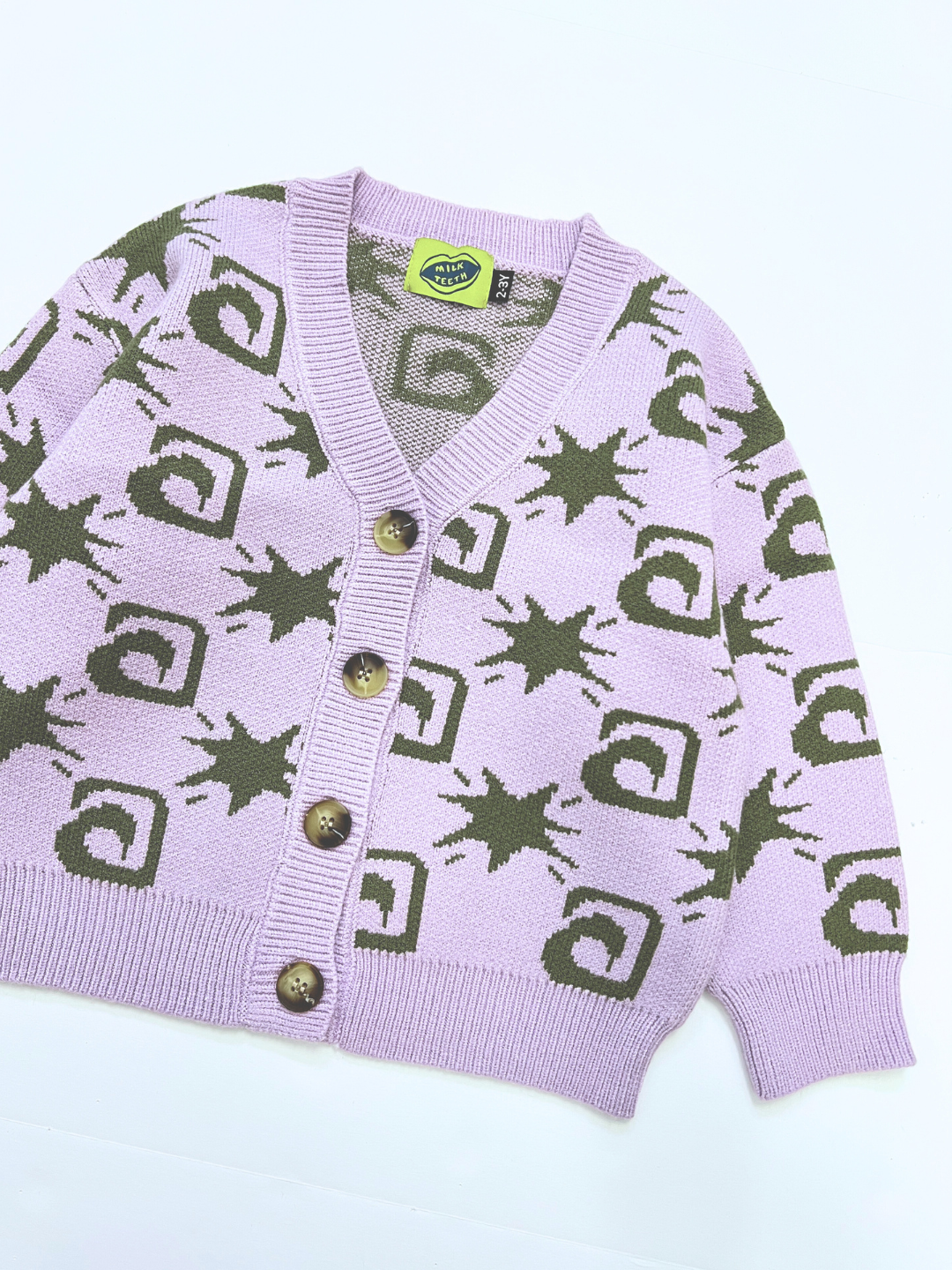 Lavender | The TRELLIS CARDIGAN is a lavender sweater featuring olive green geometric and star patterns, wooden buttons, and a yellow collar tag, displayed flat on a white background.