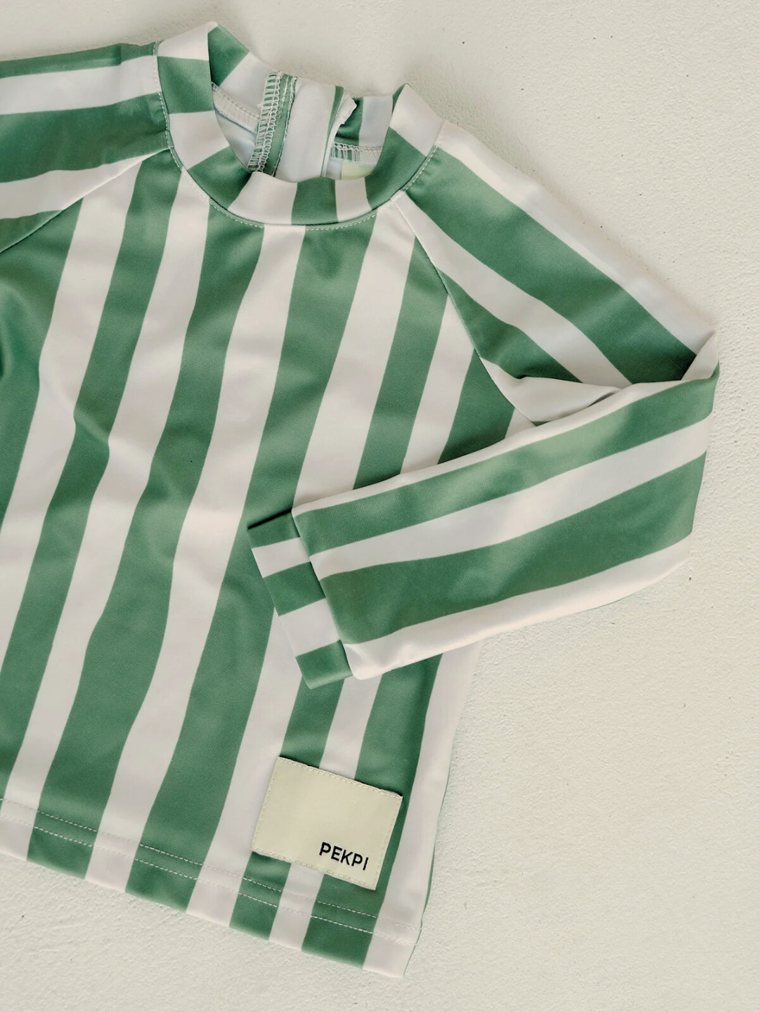 Jungle | A green and white striped SWIM RASHIE, made from recycled fabric, set against a neutral backdrop with a visible "PEKPI" label.
