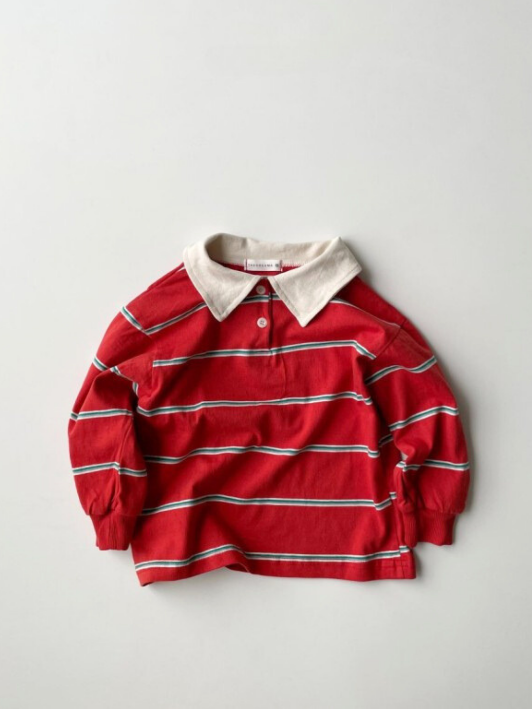 The RETRO RUGBY LONGSLEEVE features red, white, green, and navy stripes with a contrasting white rugby collar, shown flat on a light background.