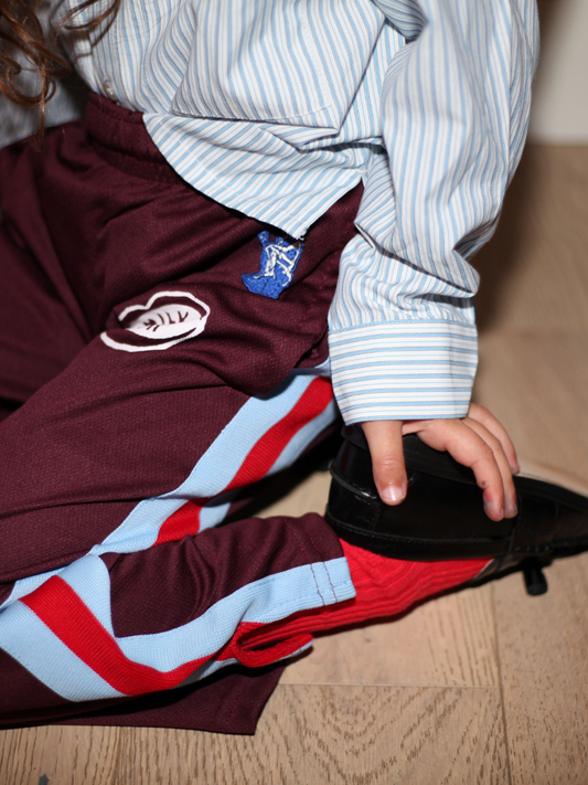Second image of RELAX x MILK TEETH PANTS in maroon, adorned with a pink "Milk Teeth" patch, featuring bold blue and red side stripes and a comfortable elastic waistband for that vintage-inspired vibe.