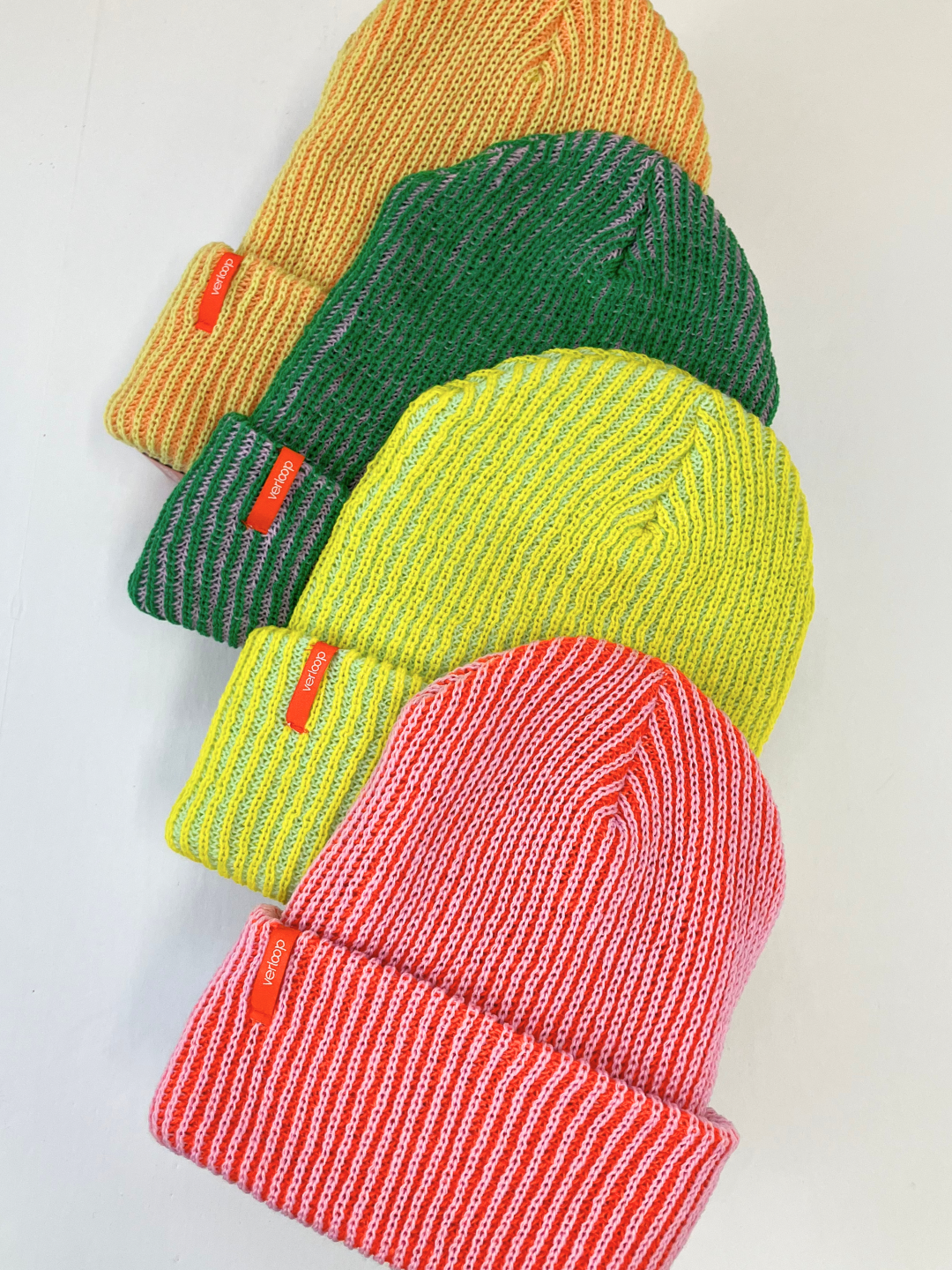 Yellow/Jade | Four ribbed knit beanies arranged on top of each other: pink, neon yellow, kely green, then peach. They have a cuff with a small red brand tag that says Verloop.