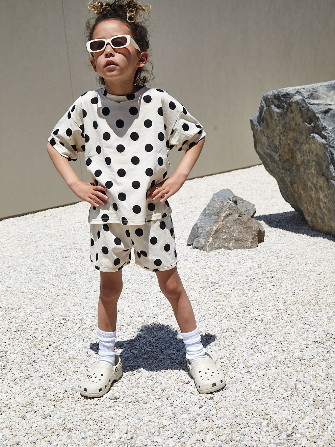 A child wearing a kids' tee shirt and shorts set in a pattern of black dots on an ecru background