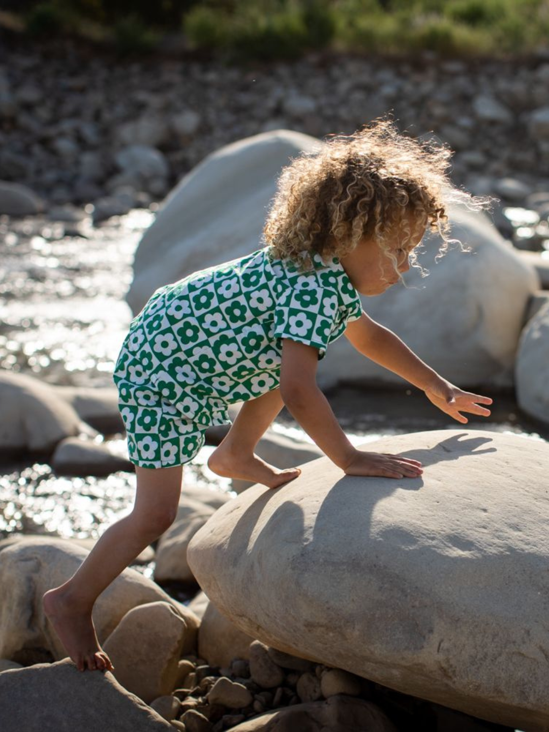 Pine | Child climbing over rocks wearing a kids' shirt and short set in a checkerboard pattern of green and white flowers