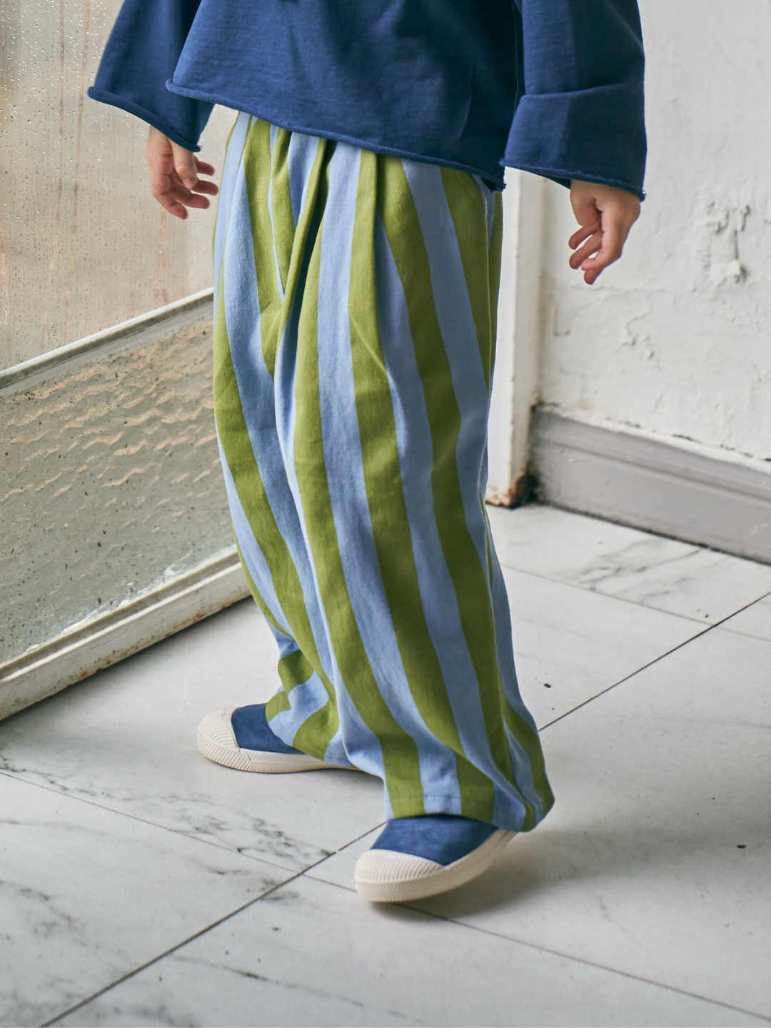 Green | Child wearing Crayon Stripe Pants with blue sweatshirt and blue sneakers.