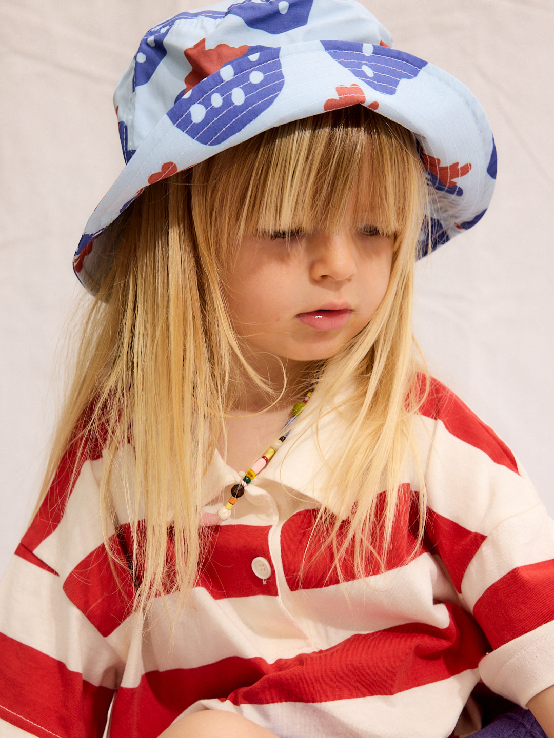 A child is wearing a Strawberry bucket hat with a red stripe polo shirt