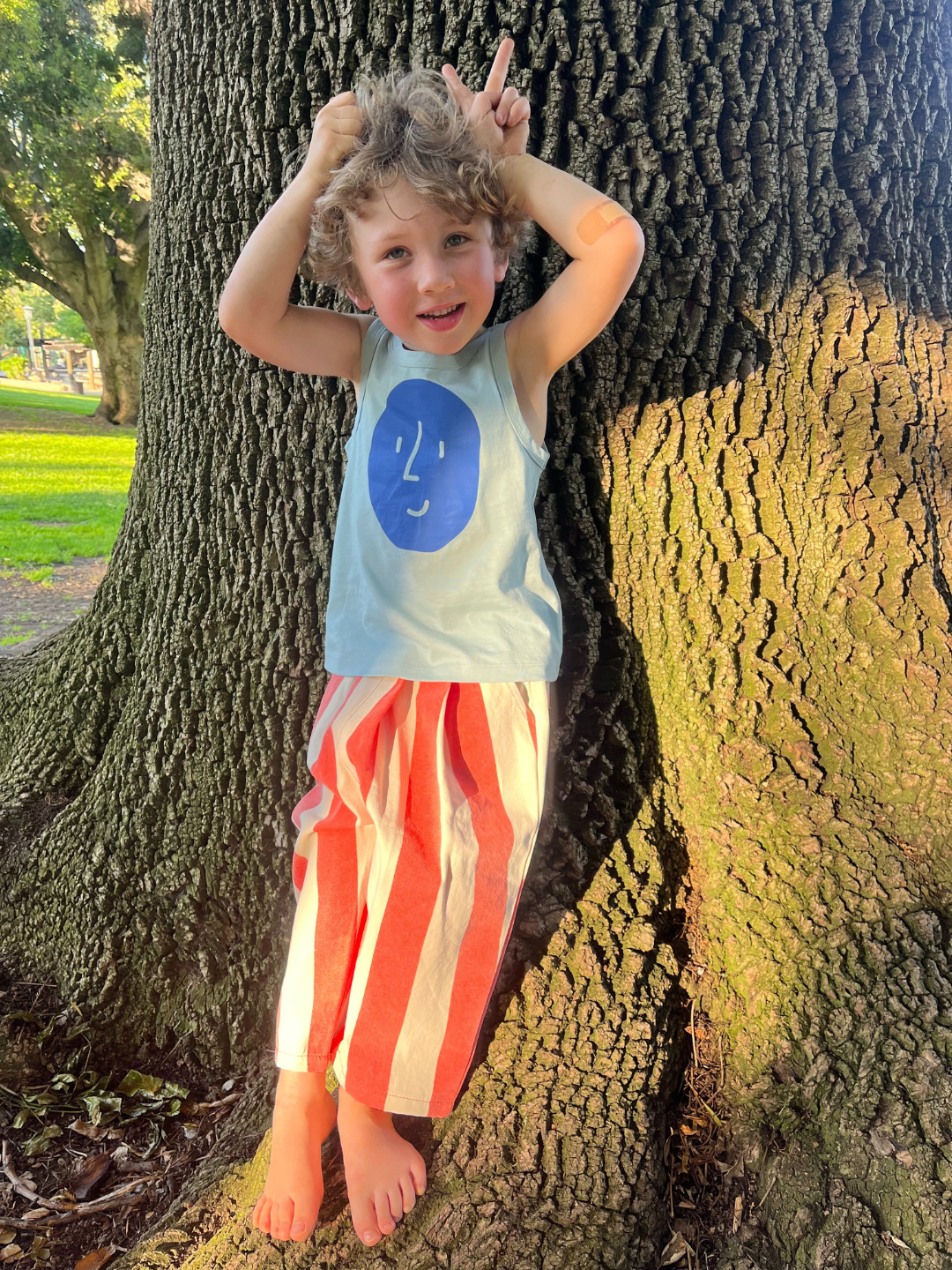 A child is wearing the Potato Face tank top with red striped pants