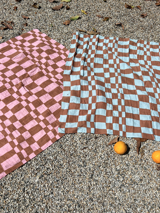 Second image of Blue Checkers | A MUSLIN SWADDLE BLANKET in a blue checkers print, made of 100% organic cotton, folded and wrapped with a white label that says “Mush Swaddle Blanket.”.