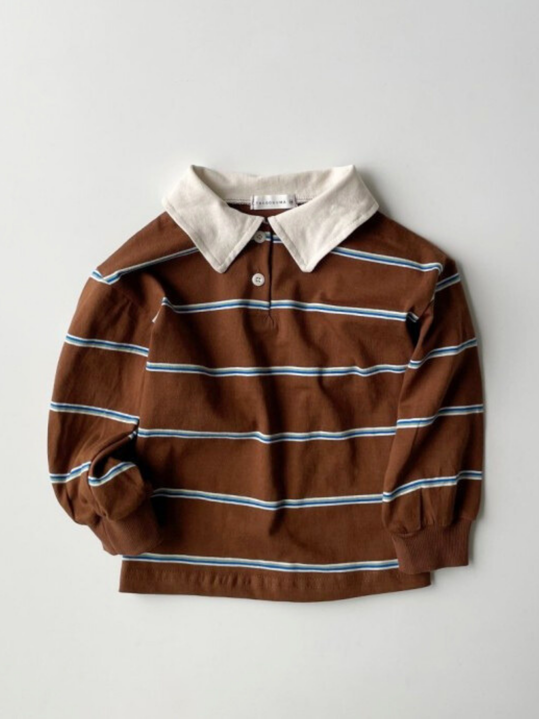 The RETRO RUGBY LONGSLEEVE features brown, white, and blue horizontal stripes with a rugby shirt collar, shown laid flat on a light background.