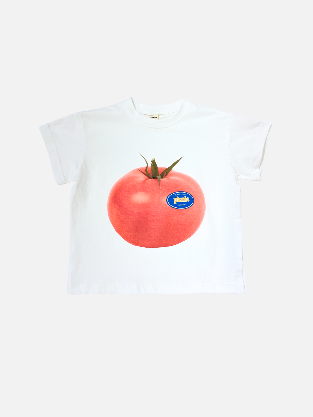 PICNIC TEE in Tomato: an oversized white cotton t-shirt from a Korean kids brand, featuring a bold tomato graphic with a blue sticker label on the front, shown against a plain background.