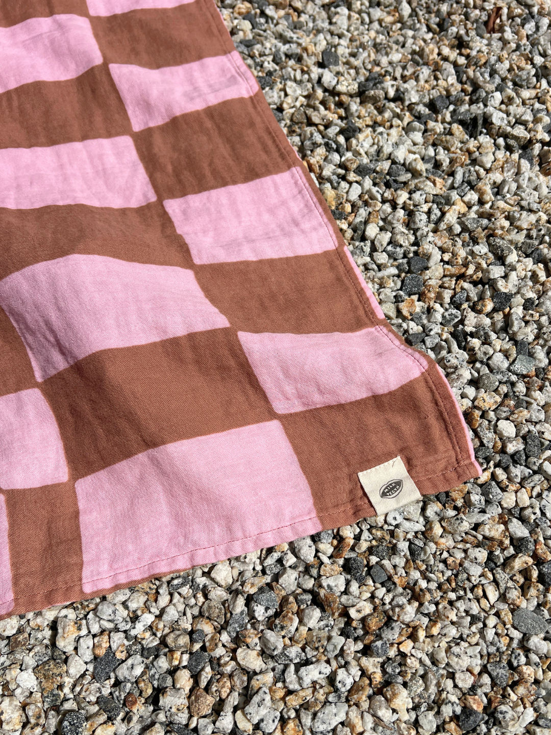 Pink Checkers | Pink and brown checkerboard muslin swaddle on a gravel surface.