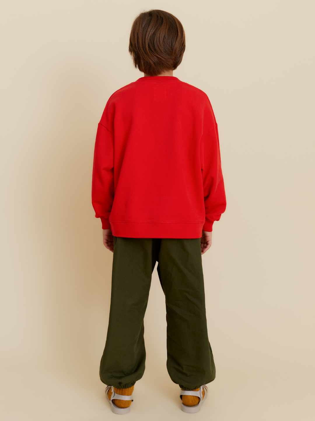 Red | Person stands with back to camera in an oversized red POTATO SWEATSHIRT, made from organic cotton, paired with green pants and yellow shoes against a plain beige background.