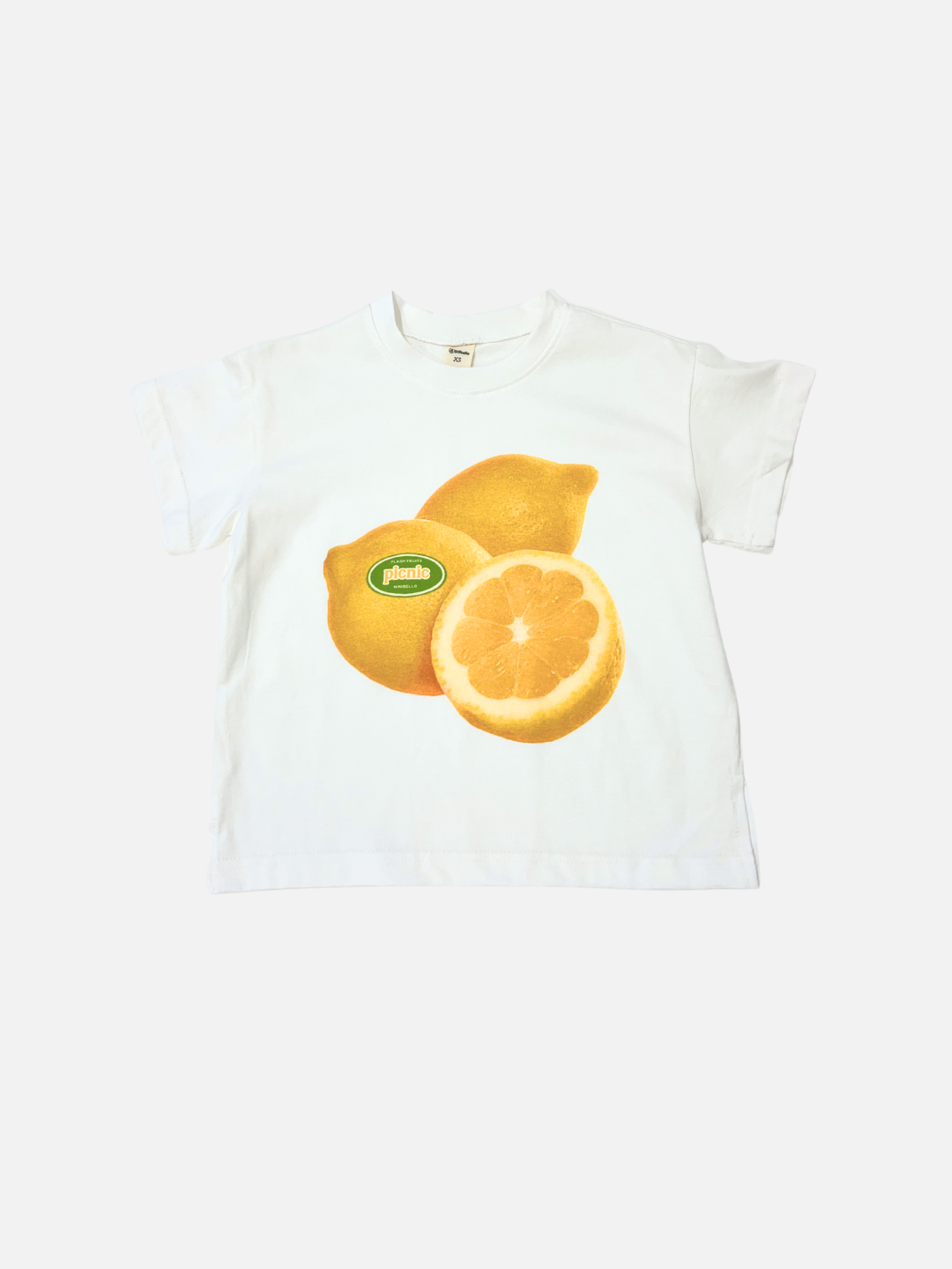 The PICNIC TEE is a lemon-colored oversized cotton t-shirt from a Korean kids brand, featuring a chest graphic of two lemons—one with a sticker, one cut in half.