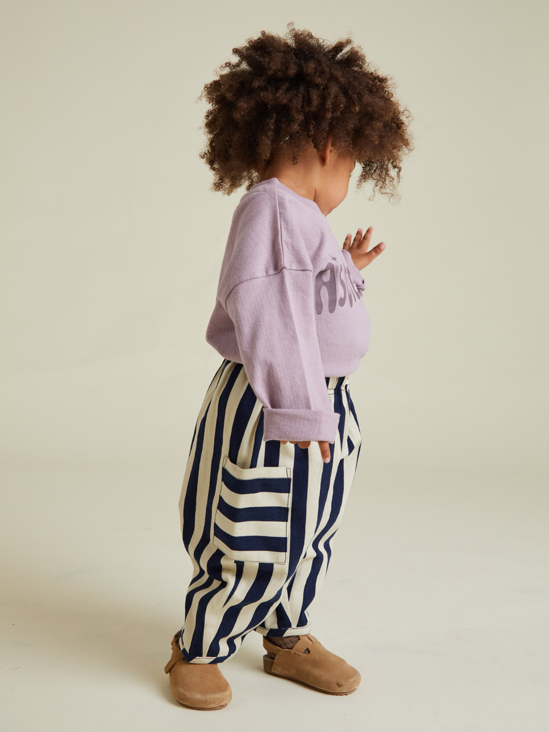 A child stands sideways in a lavender long-sleeve shirt, tan shoes, and the EMERSON MIDNIGHT STRIPE TROUSER—black and white vertical stripes—against a neutral background for a stylish look without extra cost or shipping fees.