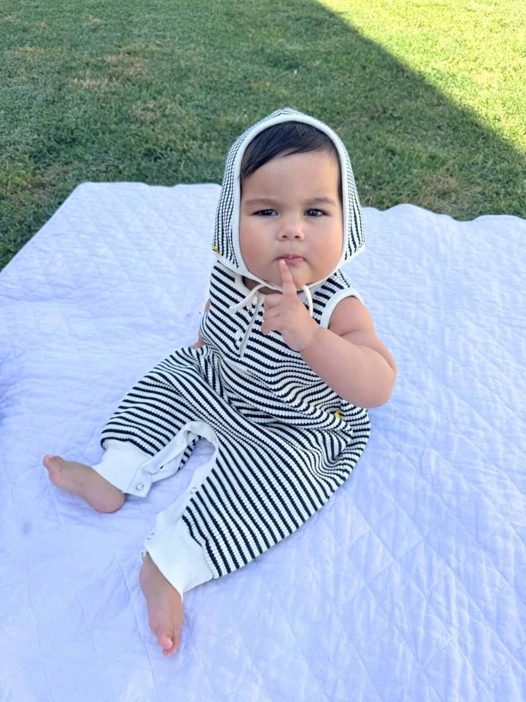 The STRIPE WAFFLE ROMPER SET, in navy, is a sleeveless baby jumpsuit made of soft waffle cotton. It features a button closure at the front, ankle snaps, and includes a matching bonnet.