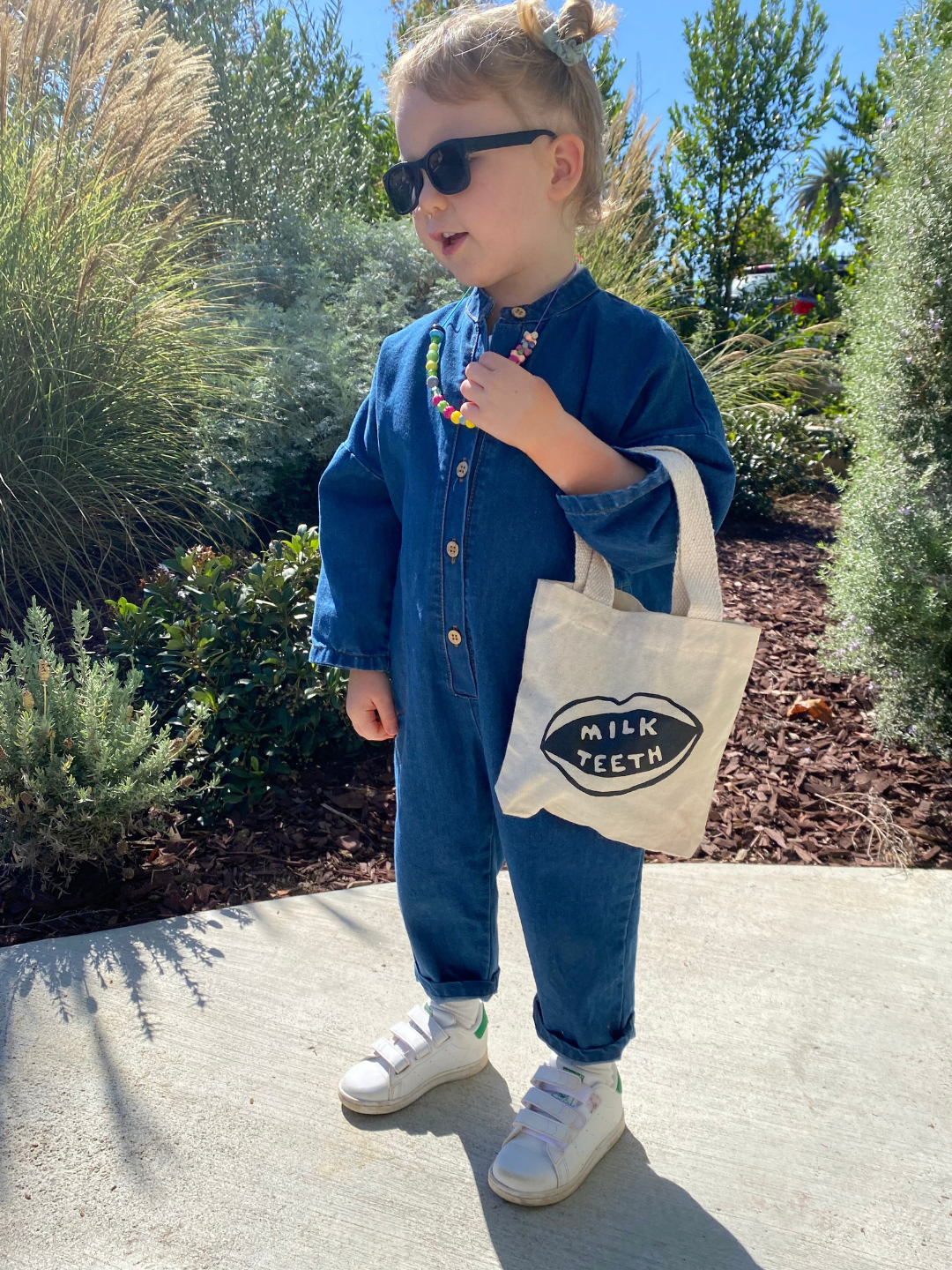 A child in a denim jumpsuit holding the Milk Teeth mini tote