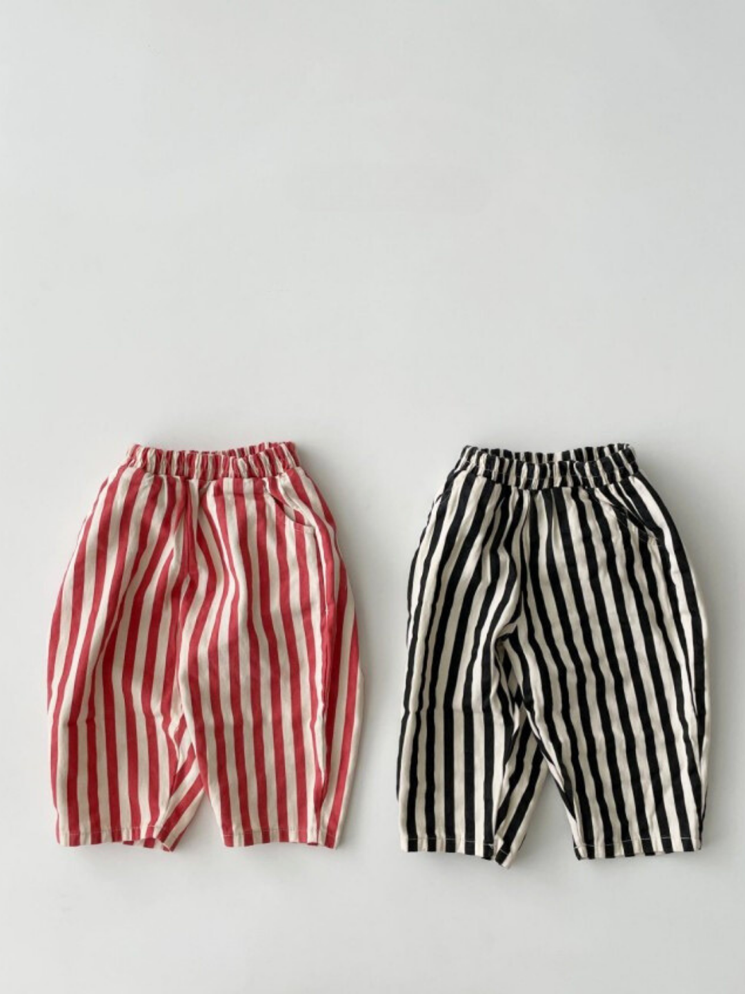 Red/Ecru | Two pairs of LICORICE STRIPE PANT for children—one red and white, one black and white—are laid flat on a light background.