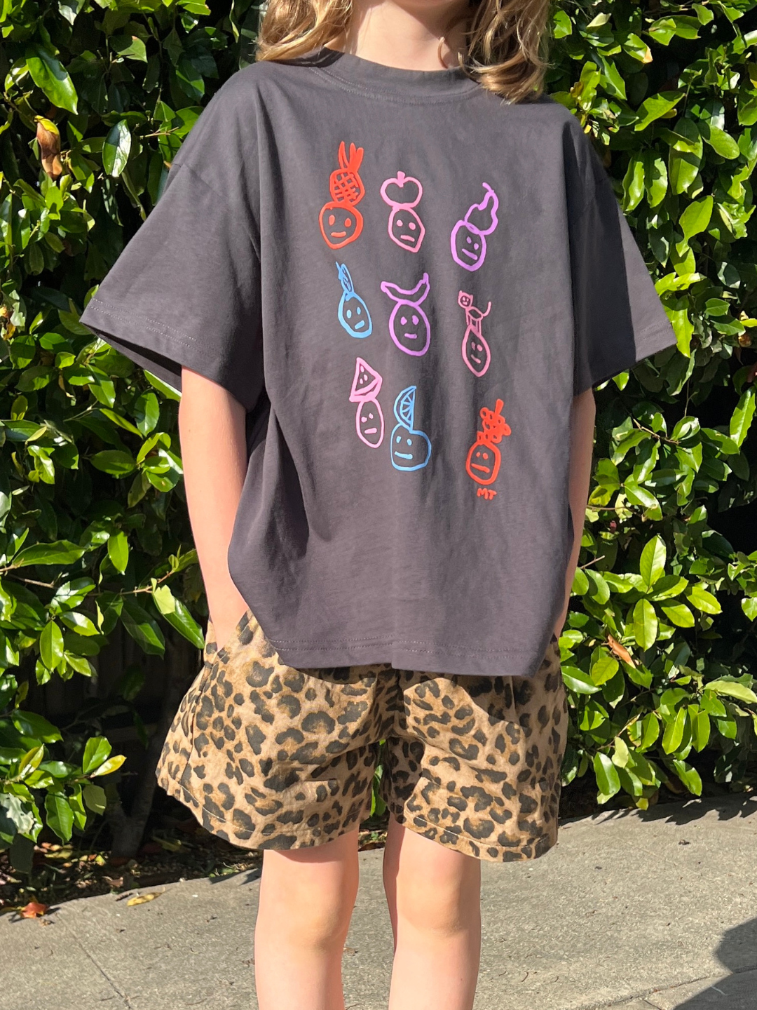 A child is wearing a charcoal fruit face tee