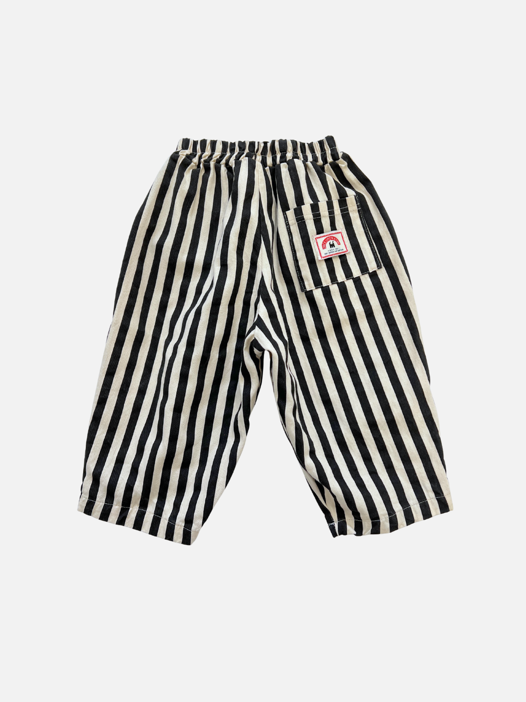 Black/Ecru | The LICORICE STRIPE PANT features black and white vertical stripes, a barrel-leg silhouette, elastic waistband, cotton twill fabric, a back patch pocket, and a small red and white label.