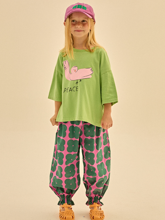 Second image of Front of Clover Pull-on Pants. Dark green clover shapes on a solid pink background. Cinched around the ankle and has an elastic waist.