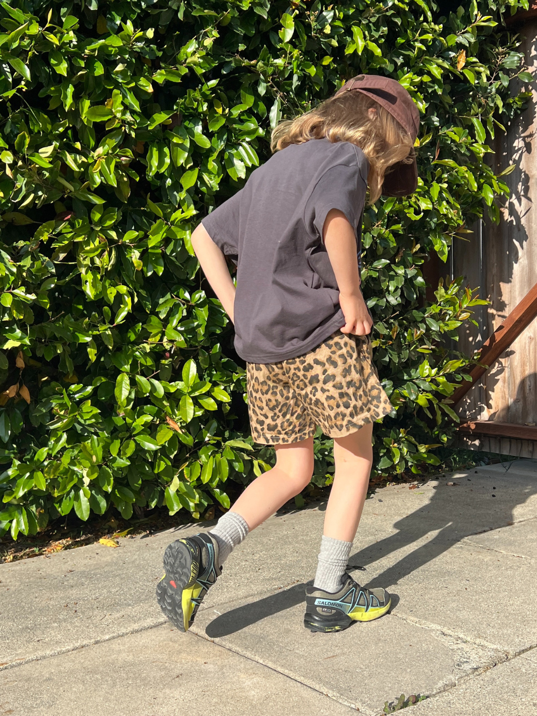 A child is wearing a charcoal tee with the Milk Teeth cap and leopard shorts