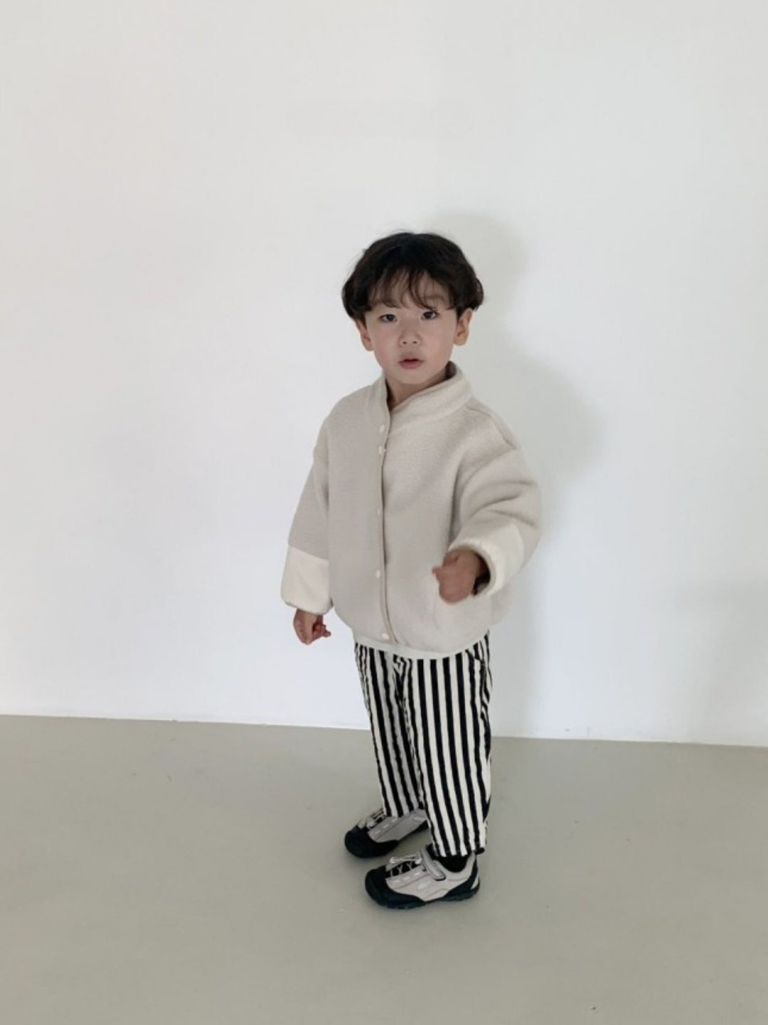 Black/Ecru | A young child stands indoors against a plain white wall, wearing a beige jacket, LICORICE STRIPE PANT with black and white stripes, and matching black and white shoes.